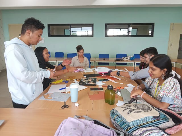 A picture of design team making a product using locally available resources. Some of the members are cutting the bits and pieces, some are sketching and others are involved in various other actions.