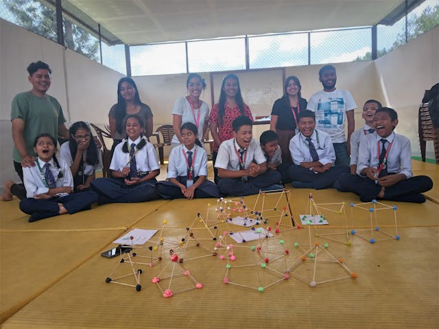 A group picture of all the children along with project members, international interns and CFC members. In front, 3D geometrical shapes made by children are displayed.