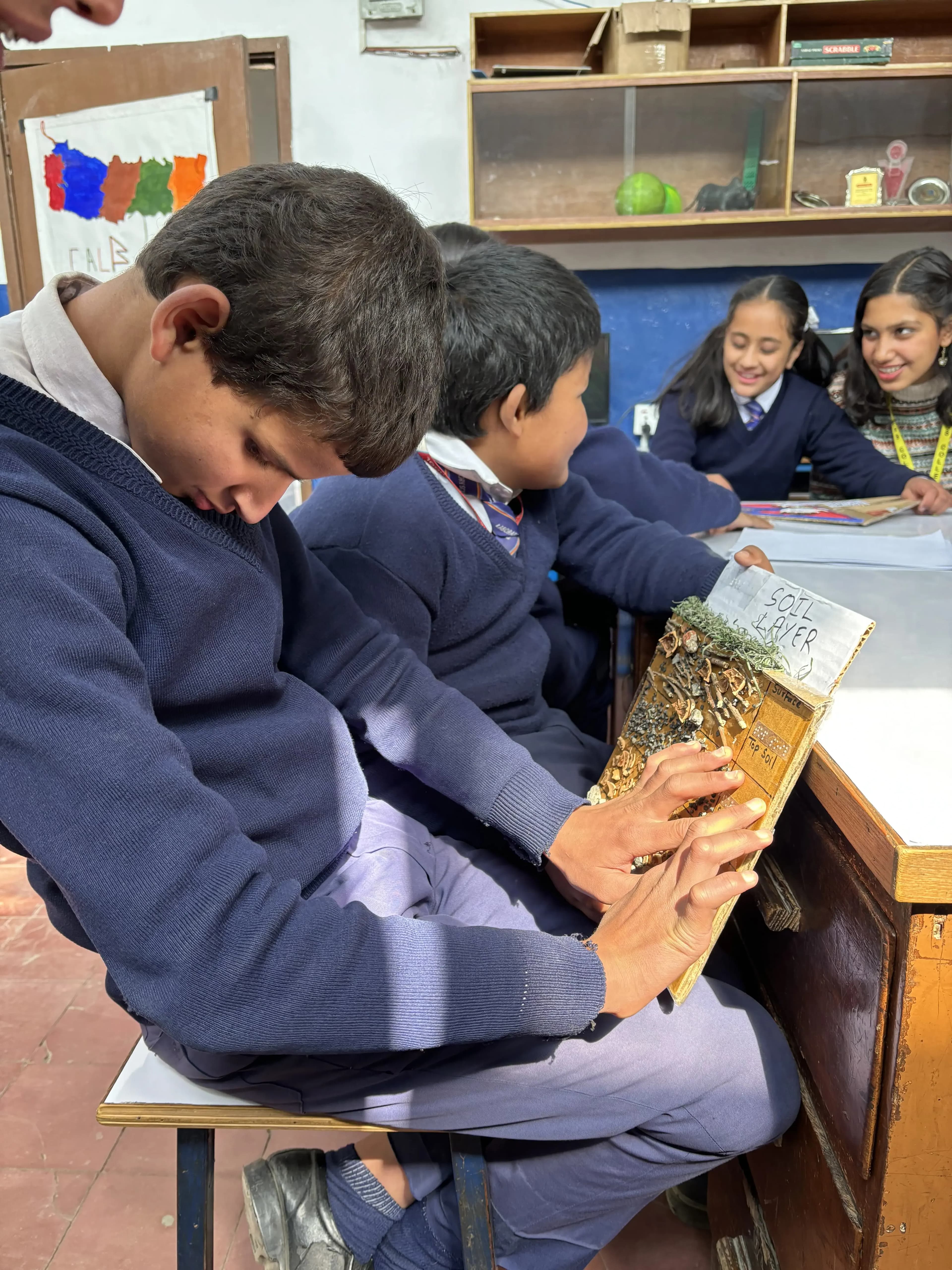 A boy is exploring the 3D model of Soil Layers. In the background his fellow colleagues and a project member is observed.