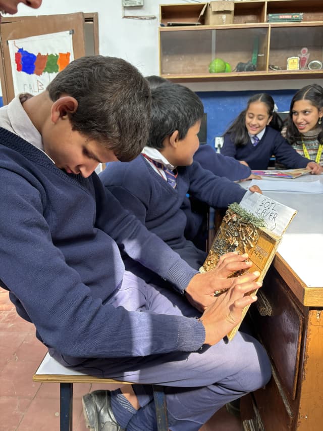 A boy is exploring the 3D model of Soil Layers. In the background his fellow colleagues and a project member is observed.