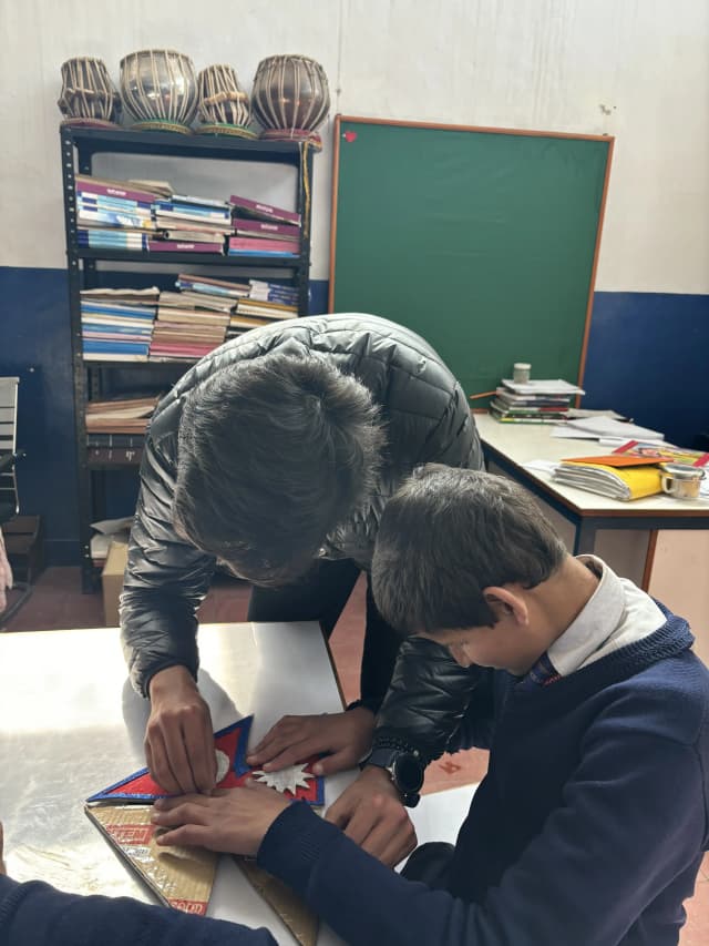 A boy is exploring a 3D model of Flag of Nepal and Project member Karmendra Shrestha is supporting him.