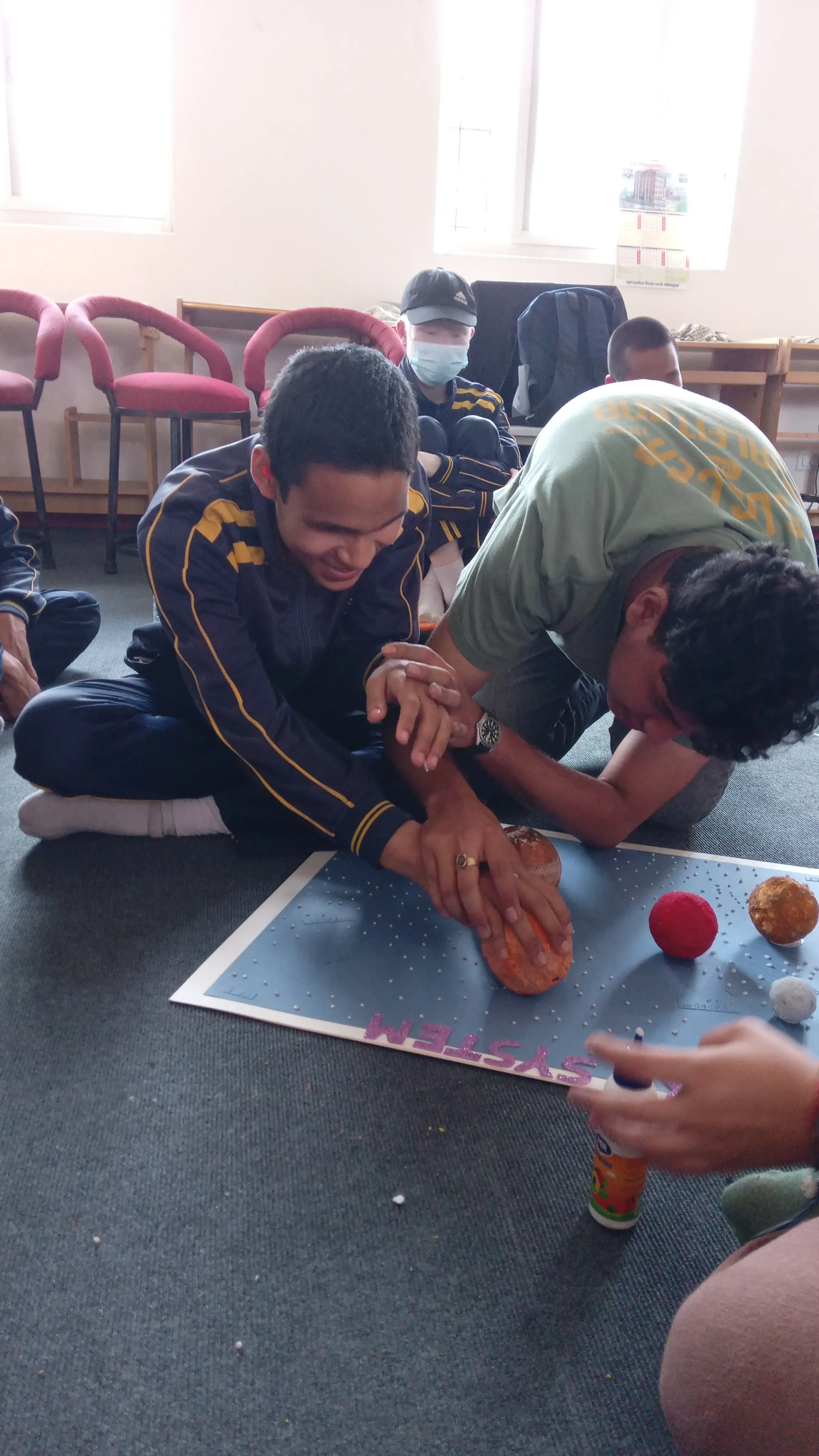 A boy is pasting a planet in its respective place on the solar system board and intern Sangam is supporting him.