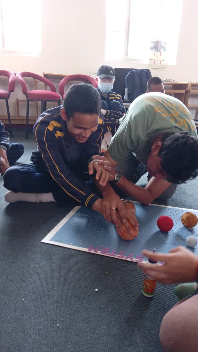 A boy is pasting a planet in its respective place on the solar system board and intern Sangam is supporting him.