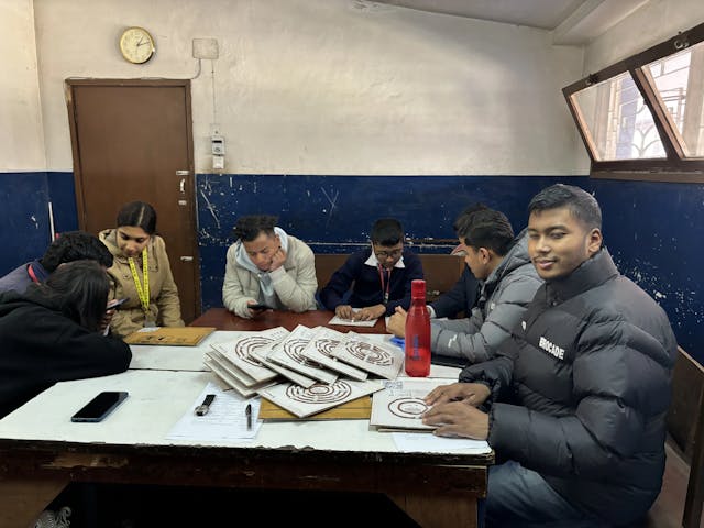 In the left, two of the project members Sweta Shakya and Sanskriti Pokharel are supporting a participant to scan QR from the CFC app placed in 3D model, in center Sambek Shahi is browsing his phone and explaining a participant. On right, project member Sangam Khadka and Founder Abhishek Shahi is observed. On the table, all the 3D models of atomic structure is observed along with bottle and mobile.