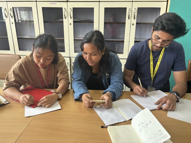 On left, Romee Jijicha is writing braille using slate and stylus, Srijana Katwal is supporting her by reading out the braille code using small slate and Karmendra Shrestha on right is noting down the points.