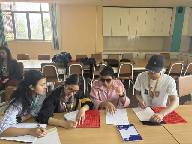 Project Member Aachal Bhatta is writing Braille with the guidance from Sabitri, Silpi Basnet is observing them and Supreme Khadka is putting the paper on slate.