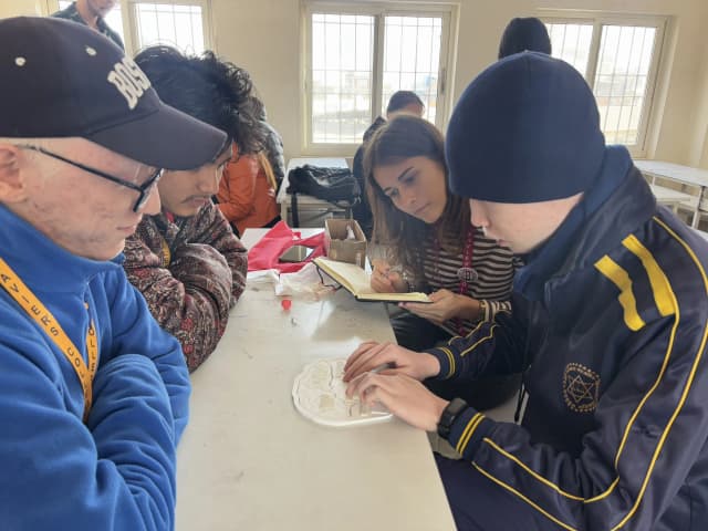 A picture of a male student with visual disability touching the 3D model of parts of brain. Gala Cervera is taking note of the student’s feedback. Project members Joon Shakya and Pralov Malla are observing the student.