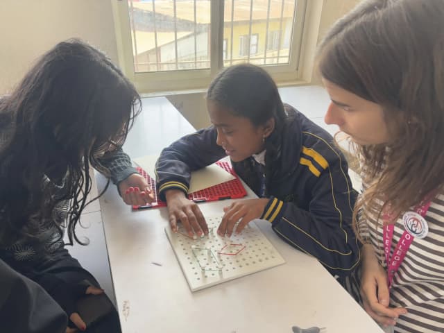 A picture of a female student with visual disability interacting with the 3D geometrical board. Project member Bhumika Shrestha and Gala Cervera are supporting her to use it.