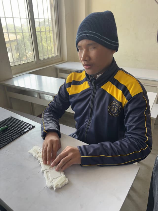 A picture where a male student with visual disability is touching the 3D map of Nepal.
