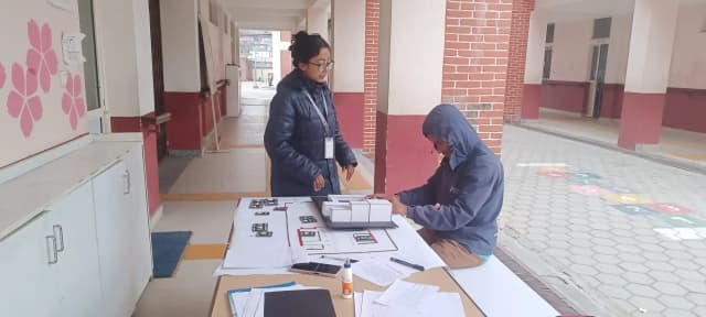 A picture of a male student with visual disability touching the 3D model of Namuna Machindra School made out of locally available resources. One of the project members, Garima Shakya is observing him.