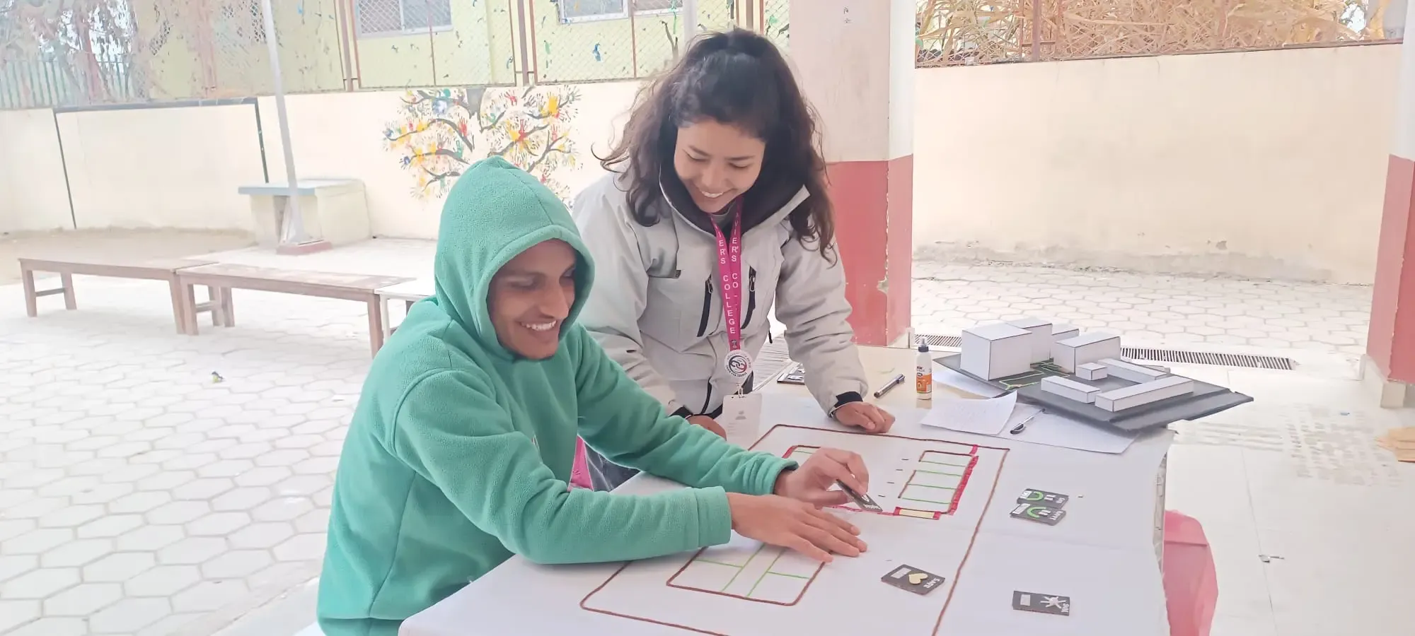 A picture of a male student with a visual disability touching the 3D tactile map of Namuna Machindra School and placing the tactile card to express his feeling and perception. Our project member, Katherine G. Silva is observing him.