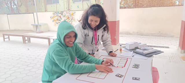 A picture of a male student with a visual disability touching the 3D tactile map of Namuna Machindra School and placing the tactile card to express his feeling and perception. Our project member, Katherine G. Silva is observing him.