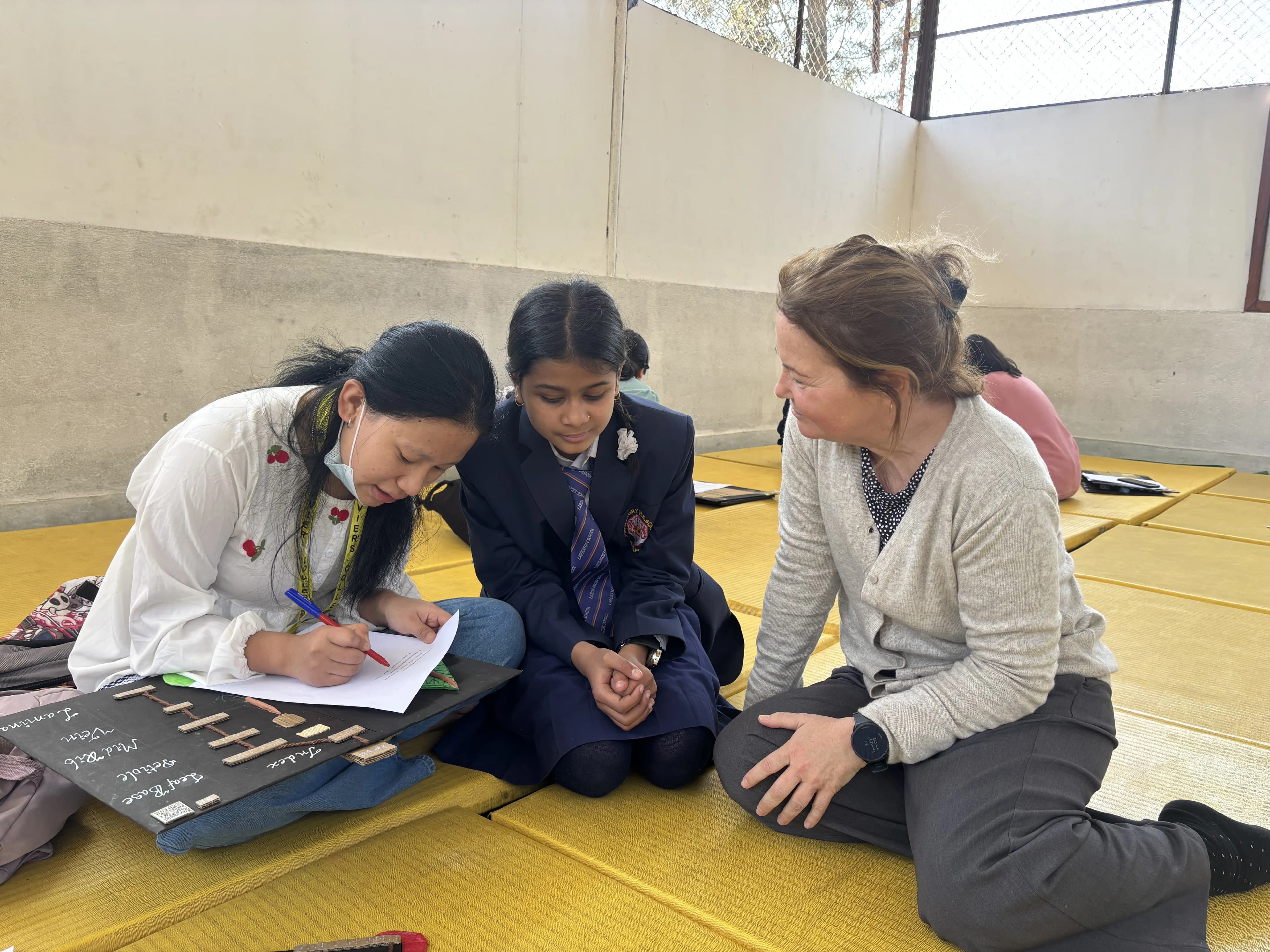 A picture showing a girl with visual disability is responding the pre/post tests administered by one of our project member Pushpakala Rai. Ana – the exchange staff is observing them.