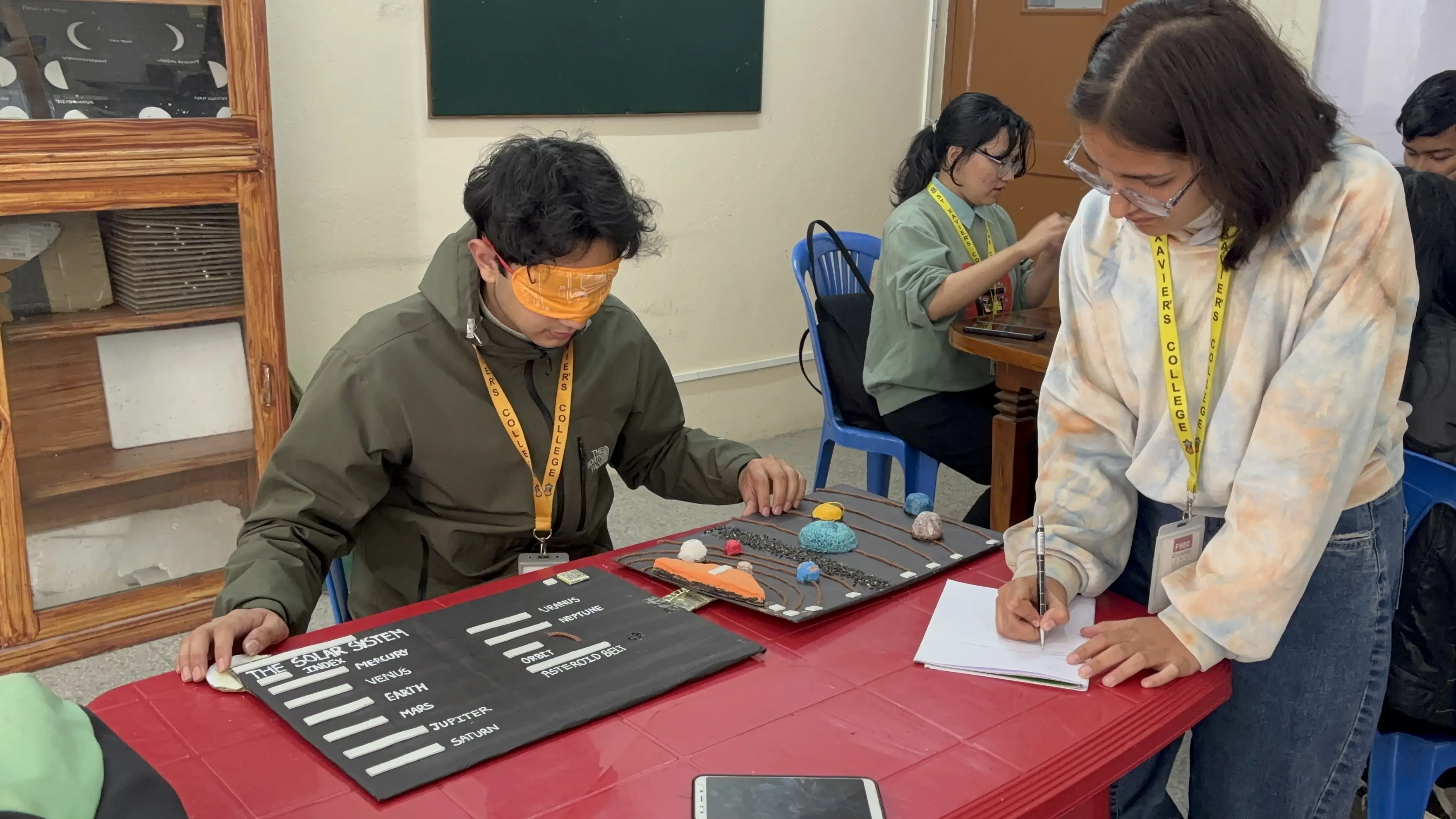 A picture where one of our project members, Supreme Khadka is exploring the 3D model of Solar System being blindfolded. Project member, Aachal Bhatta is taking the note.
