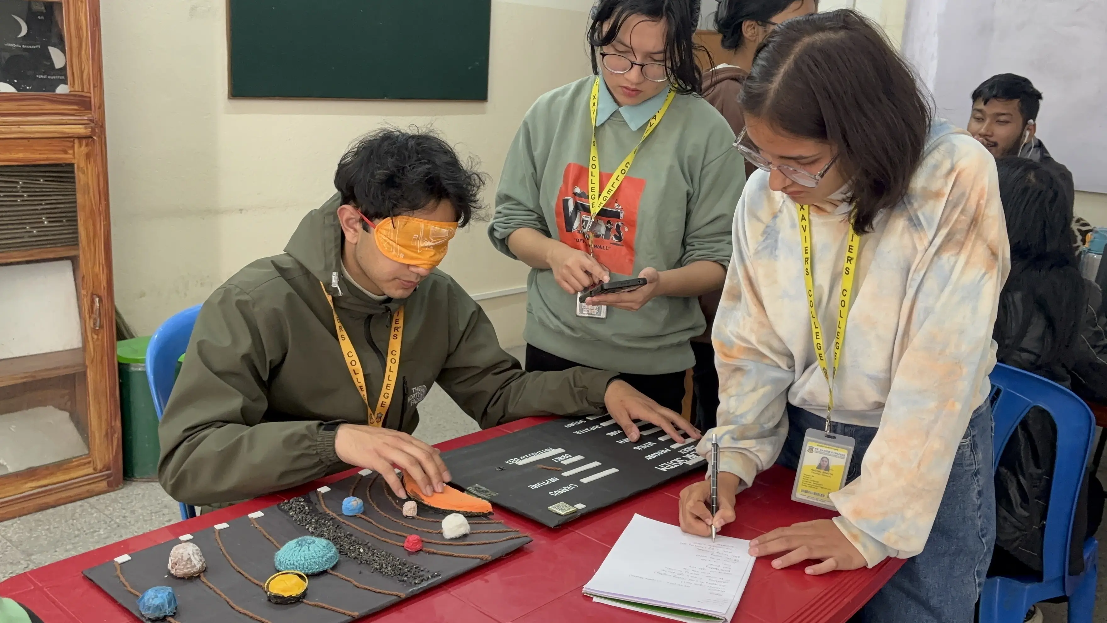 A picture where one of our project members, Supreme Khadka is exploring the 3D model of Solar System being blindfolded. Here, project member, sanskriti Ghimire Khatri is supporting him to listen to audio description and Aachal Bhatta is taking the note.
