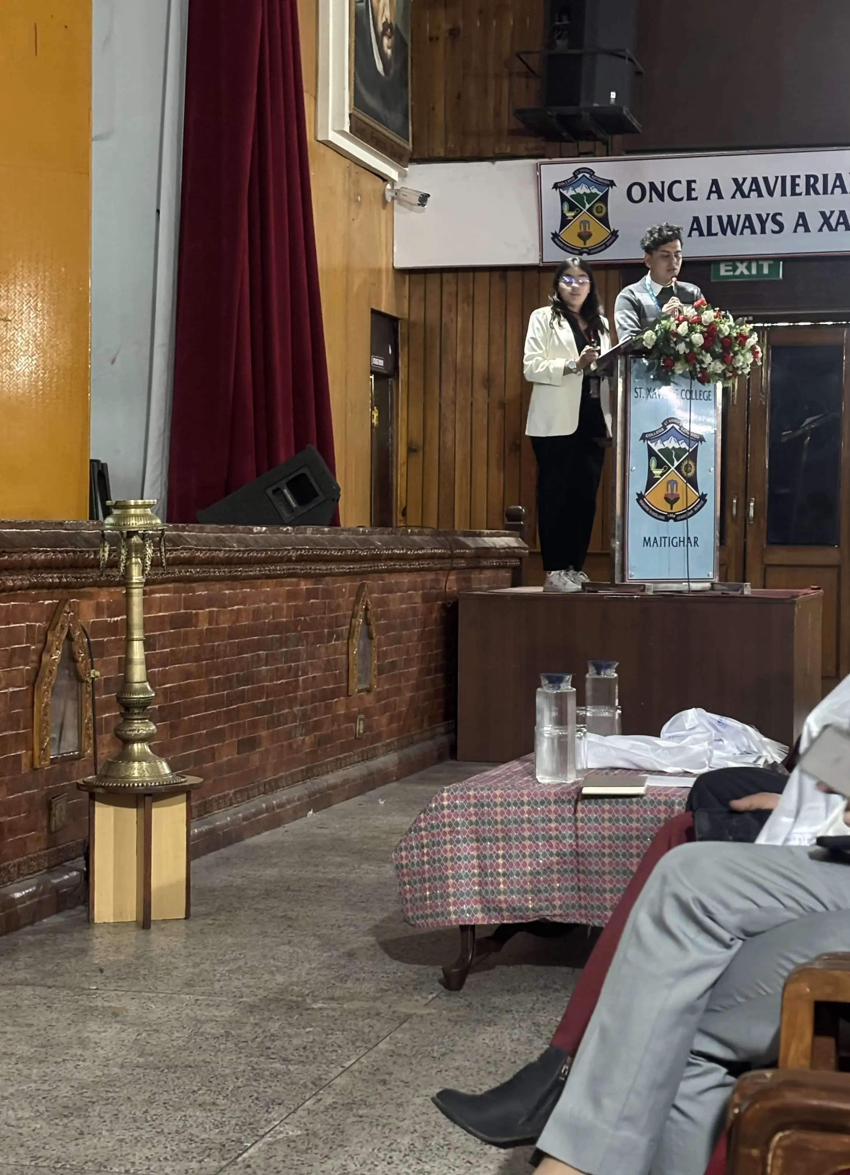 Our Public Relation & Philanthropy Officer, Mr. Sangam Khadka and Design Support Officer, Ms. Khushi Subedi, presenting about Project Wings to Dreams from the podium.