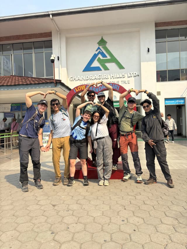 A group picture of 8 individuals posing with a hand gesture of a heart including Mr. Alfonso Xosé González Cabarcos and his 4 Spanish students along with CFC members. In the background, there is a photo stand where it is written 'I love Chandragiri'.