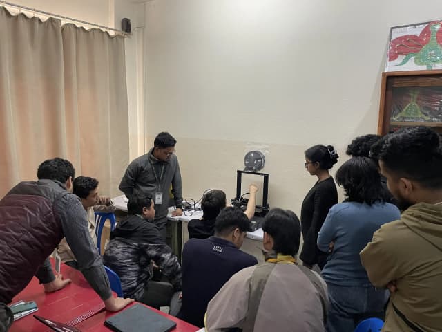 Mr. Miquel Cañada is explaining about the FDM 3D printer and the participants are listening to him. In the background FDM 3D printer can also be observed.