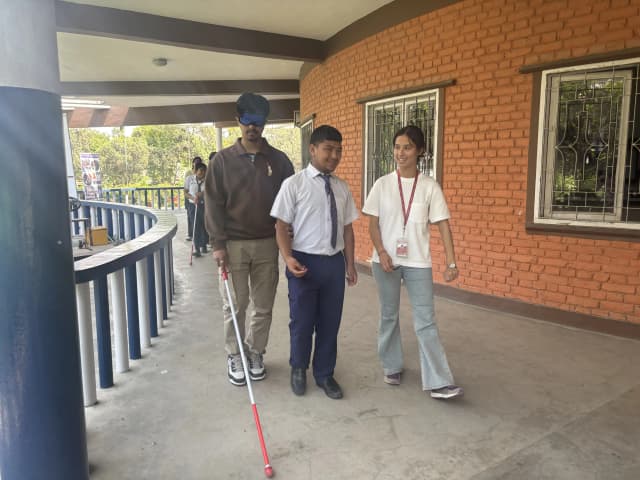 One of the participants with visual disabilities is guiding his blindfolded pair throughout the premises of the school. Another pair from the group is observing them.