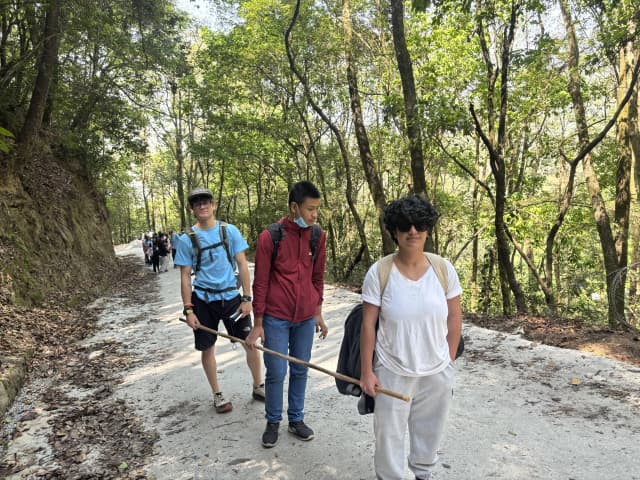 Two of the pair guides are holding the long stick in either sides and a participant with visual disability is holding it in between. In a background, a beautiful scenery is observed.