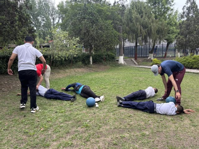 4 of the students with visual disabilities are learning the technique to defend the goalball. Other facilitators and project members are guiding them.