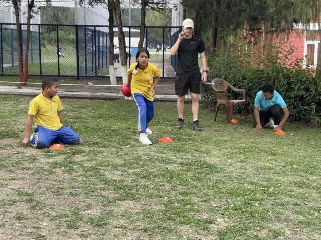 A goalball team of 3 students with visual disabilities, where one of the female student is about to throw the sound ball.