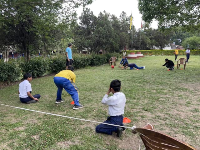 A full court of goalball is seen where both the team with 3 members with visual disabilities are positioned. In one side, a team member is diving to defend the ball. In the background, some of the project members, students and Spanish interns are observed.