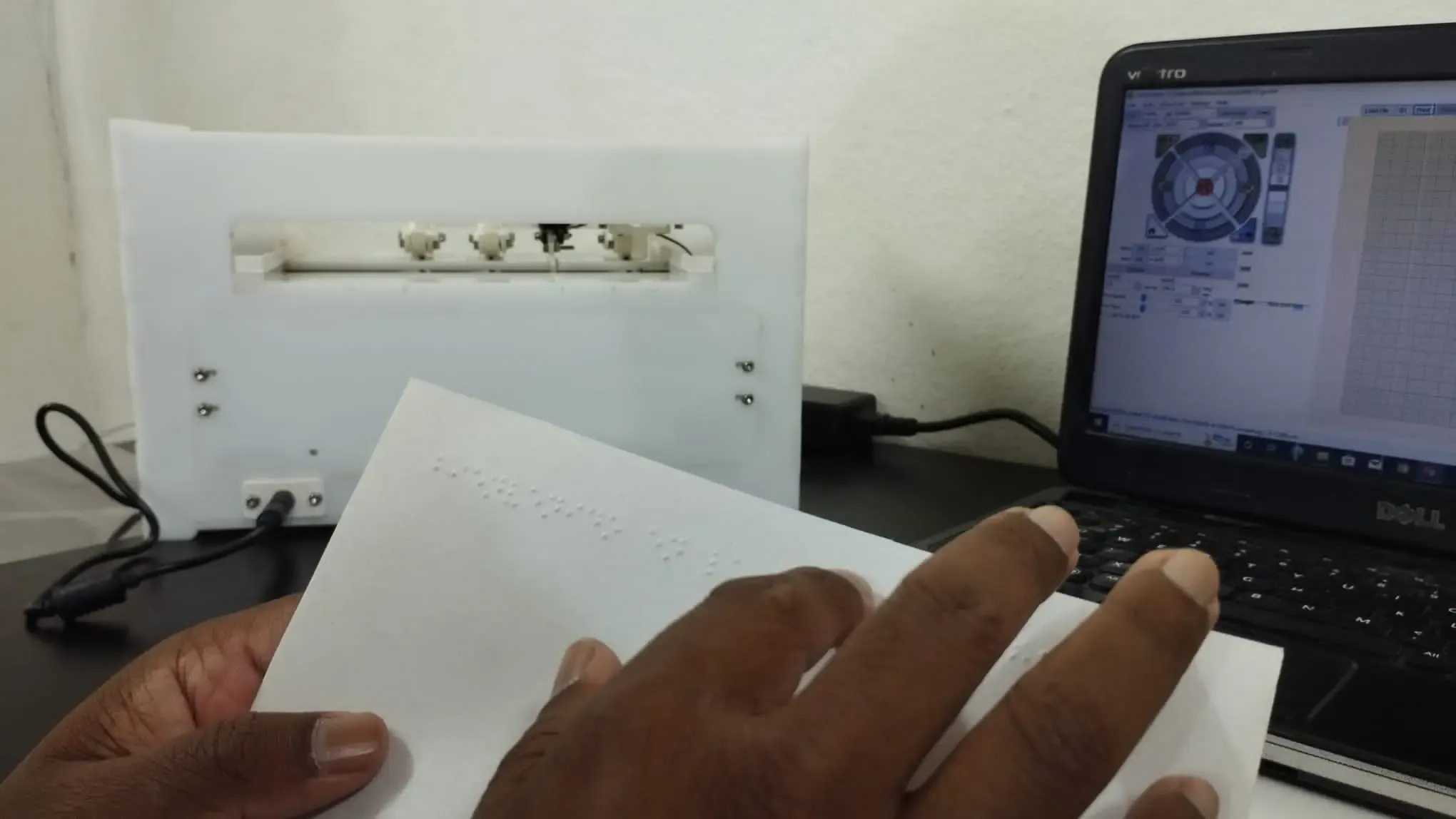 Our Founder, Mr. Abhishek Shahi is touching the printed braille paper. In the background, a braille printer and a laptop can be observed.