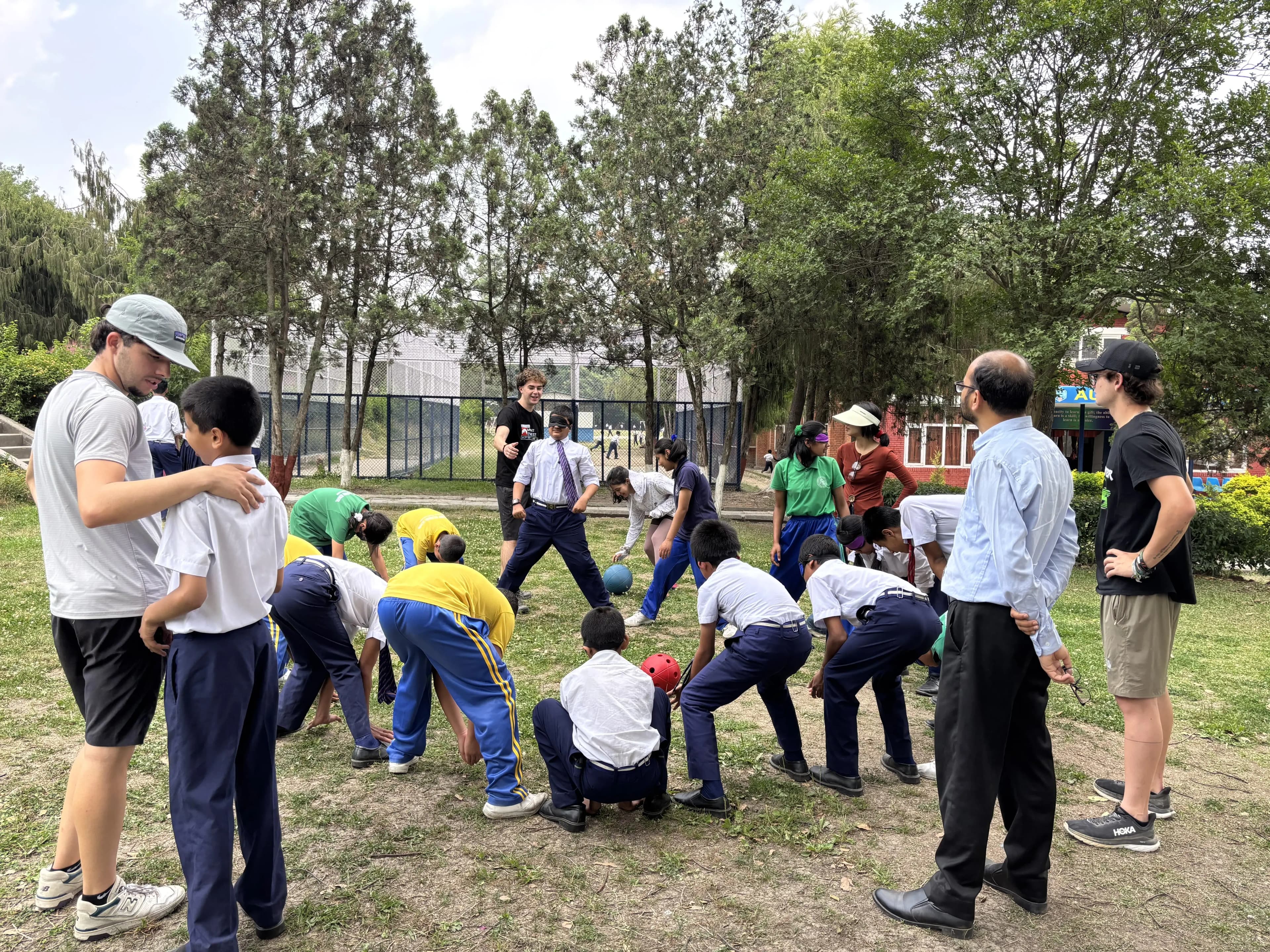 An image where children with visual disabilities are standing making a circle, playing a sound ball. Even Spanish interns are observed in the picture.