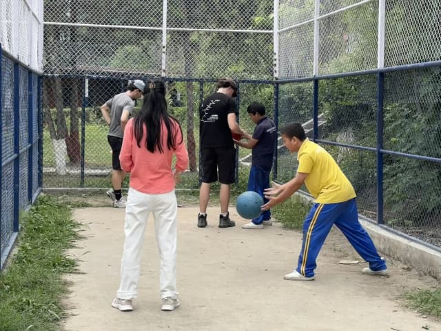 Two of the male participants with visual disabilities are learning to throw the sound balls. One of the Spanish interns is teaching a male participants to throw the ball.