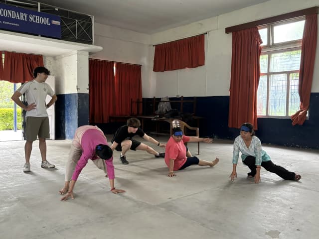 One of the Spanish interns is teaching the teachers defense techniques that is used in Goalball. Another Spanish intern is observing them.