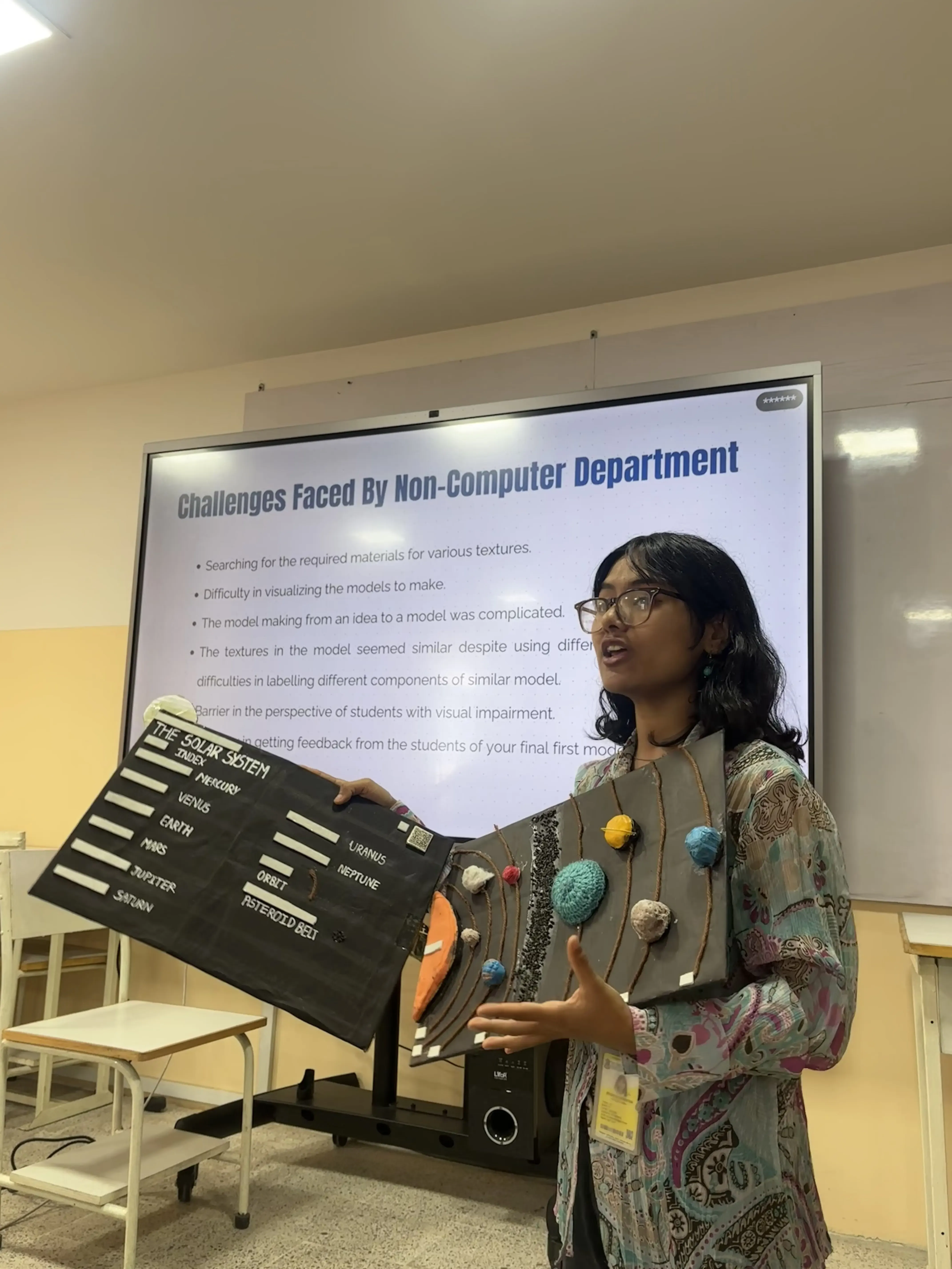 Public Relation Officer, Ms. Bhumika Shrestha is presenting holding a 3D model of Solar System. In the screen, “Challenges faced by non-computer team” is displayed along with its sub points.