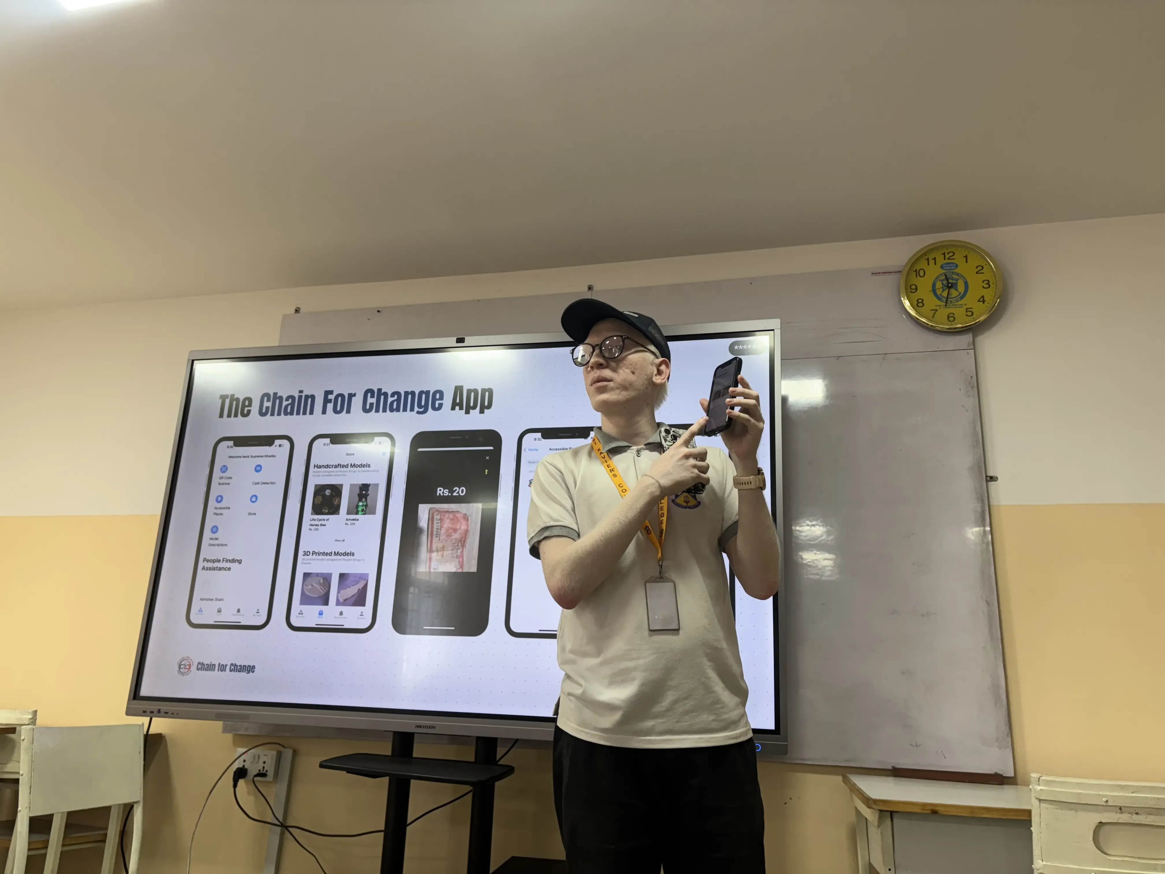 IT & Creative Specialist, Mr. Joon Shakya is explaining about CFC app holding a mobile phone. On the screen, “The Chain For Change app” is displayed along with its features.