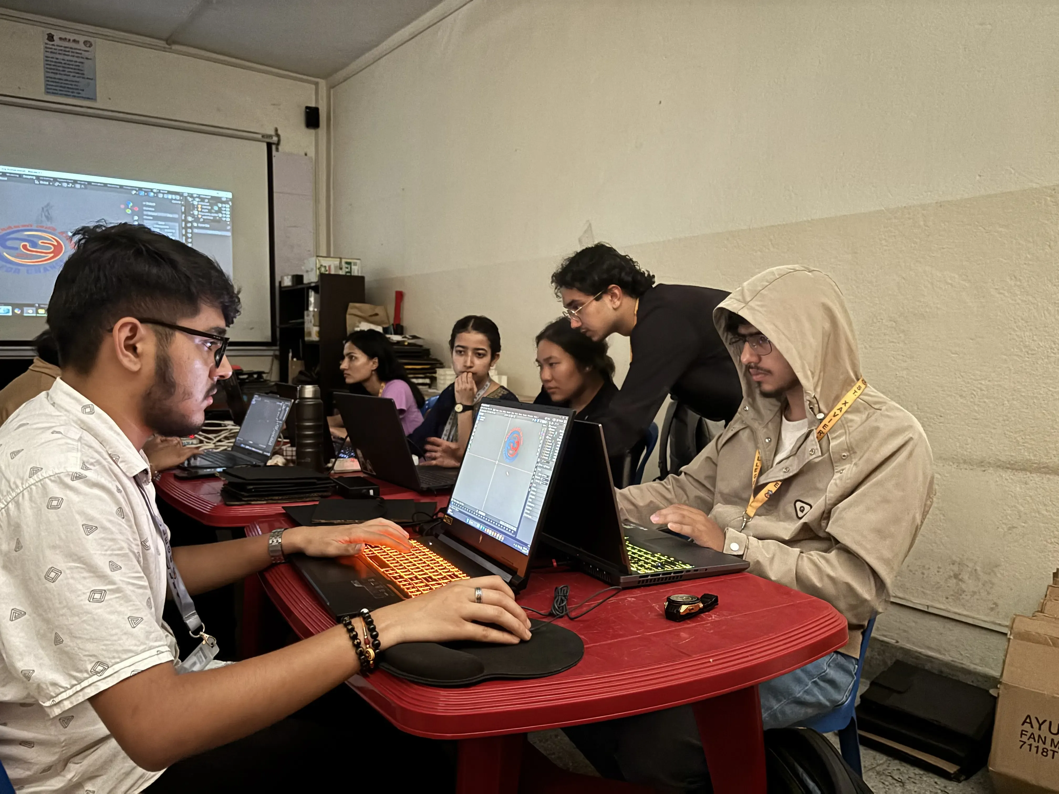 Lead of the Computer Department (2024/25), Mr. Supreme Khadka is explaining one of the new project members, Ms. Muhingma Limbu. Other participants are observed using their computers. The logo of CFC is being projected in the screen.