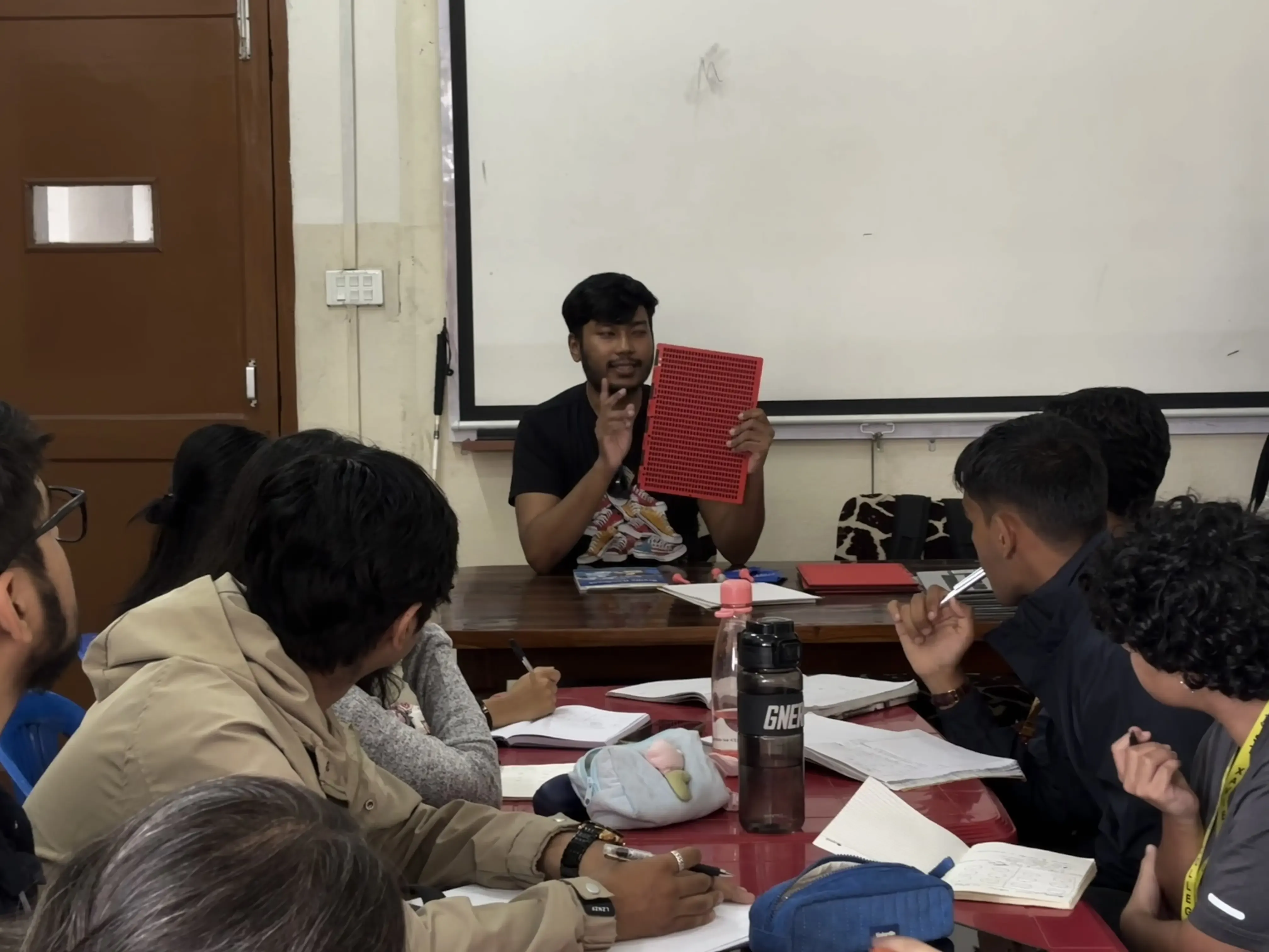 The facilitator of the event Mr. Abhishek Shahi is holding a slate in his hand and explaining about it. The participants of the event are listening to him.