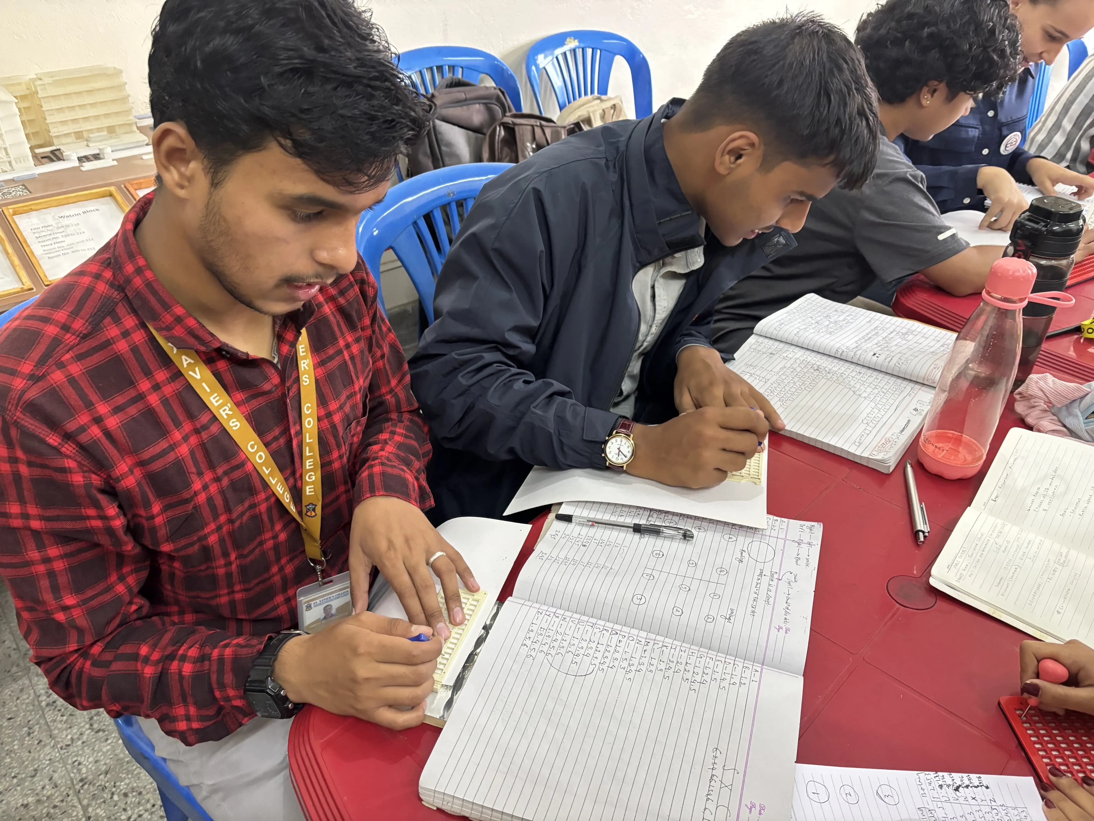 Two of the male project members (2025/26) are writing in braille using braille slates and styluses.