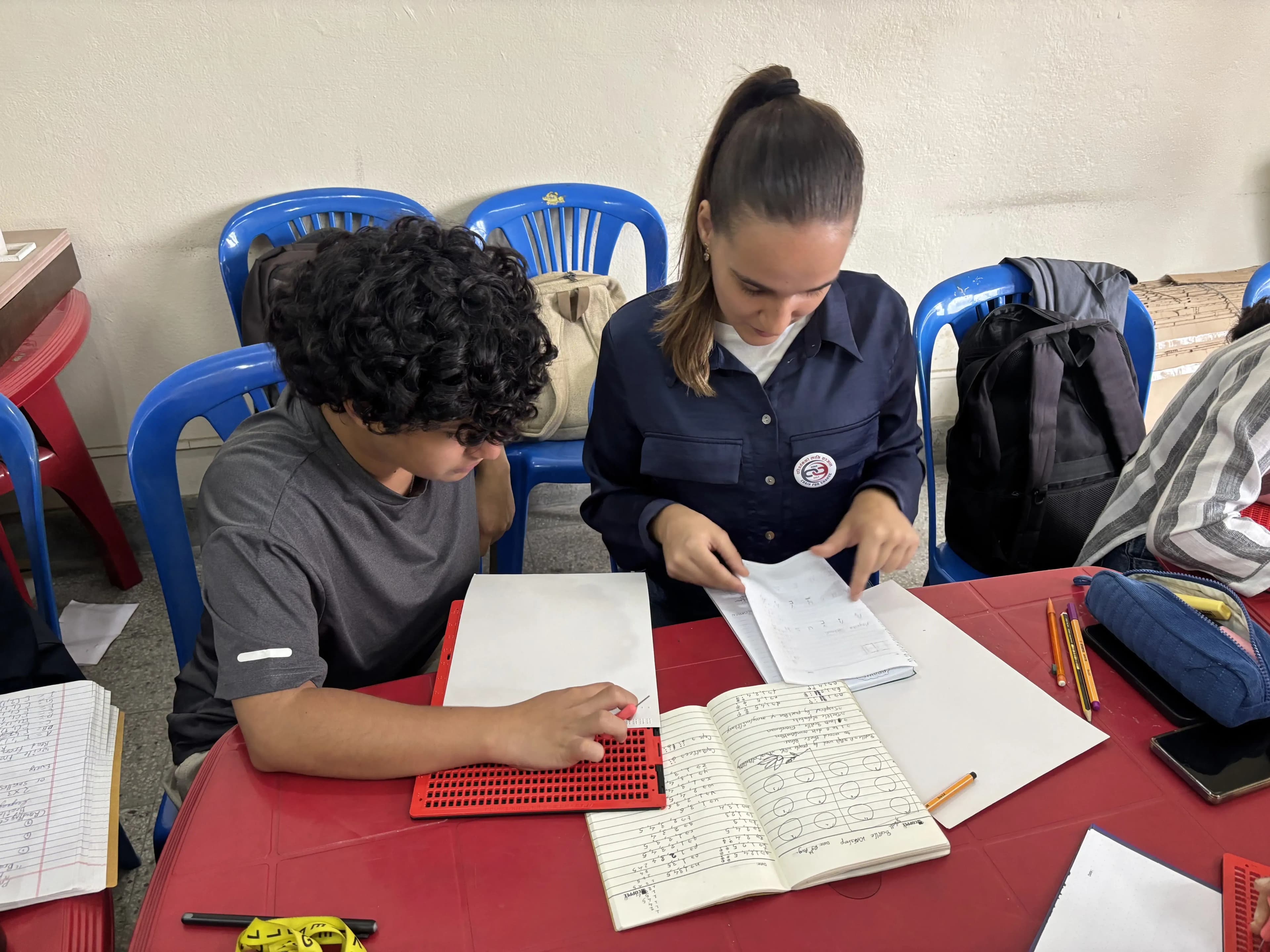 Two of the female participants of the workshop are referring to their respective notebooks and practicing to write using slates and styluses.
