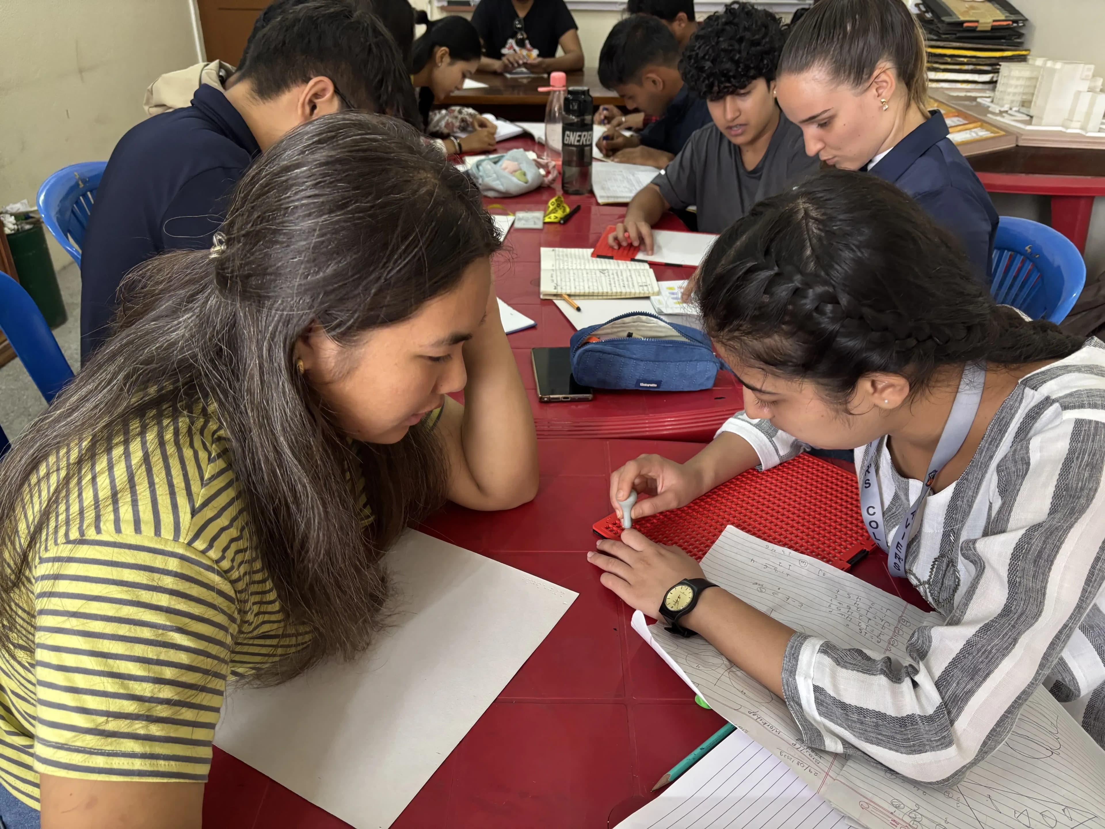 One of the female participants is supporting other female participant to write braille.