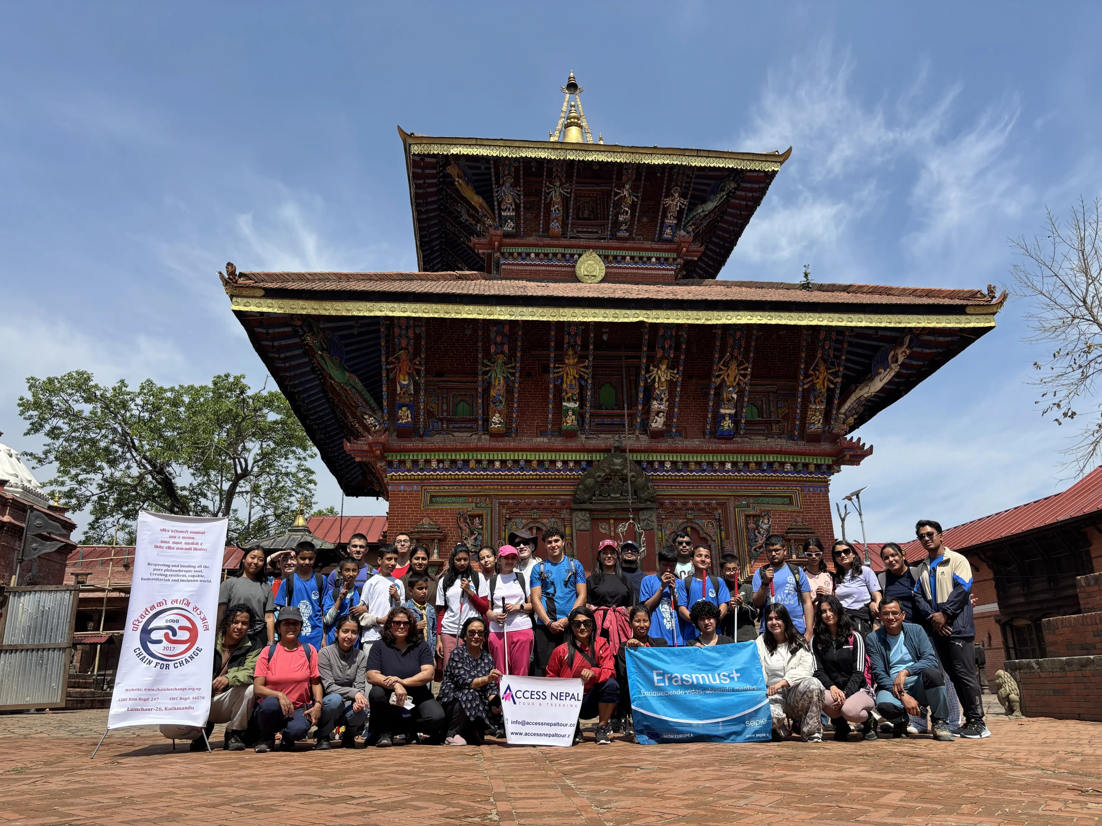 Group photo of participants from the guiding and mobility training posing with banners in front of a traditional multi-tiered temple building under a bright blue sky.