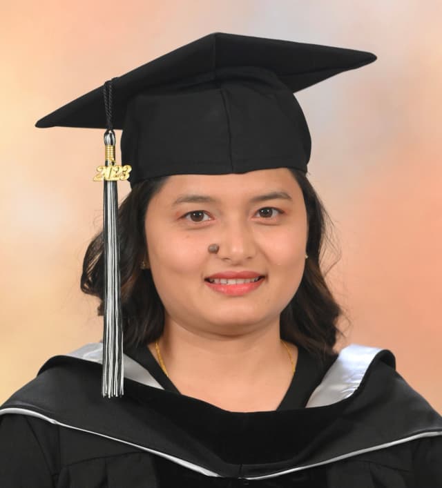 Young woman with light-brown skin and shoulder-length dark hair, wearing a black graduation cap with a “2023” tassel and a black gown with a light-colored trim, smiling slightly against a soft beige background.