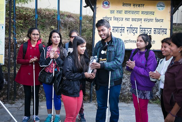 The Founder and Director Mr. Abhishek Shahi of Chain For Change providing white cane to one of the blind hiker just before hiking. In the background other co-founders, organizing team and participants are observed with the banner of Shivapuri Nagarjung National Park.