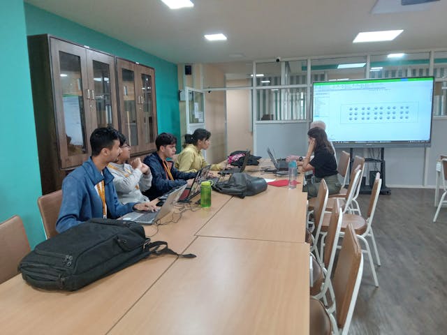 A picture where 6 dots of braille is displayed in the big screen, two of the dedicated team are looking at it and others are working in their laptops.