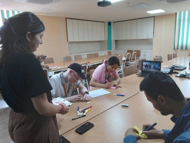 A picture where, three of the 3D design team are writing on sticky notes and the intern design instructor is observing them.